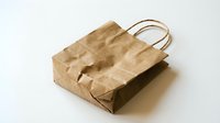 Crumpled brown paper shopping bag with twisted handles isolated on white background for eco-friendly retail packaging and sustainable commerce designs.