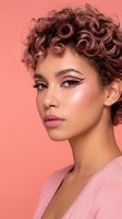 Young mixed-race woman with curly hair and dramatic winged eyeliner makeup on coral pink background for beauty and cosmetics advertising campaigns.