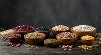 Assorted legumes and grains in wooden bowls on rustic table. Variety of beans, lentils, chickpeas and cereals for healthy cooking and nutrition.