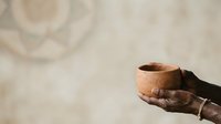 Weathered hands holding an empty terracotta cup against a neutral textured background, conveying themes of poverty, charity, need, and humanitarian aid.