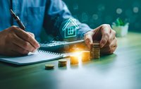 Businessman calculating mortgage loan with house icon and coins on desk for real estate investment planning and financial analysis.