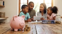 African American family with two children learning about money management and savings with piggy bank and coins on wooden table at home.