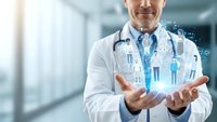 Male doctor in white coat holding holographic medical icons and digital healthcare symbols in modern hospital corridor representing telemedicine innovation.