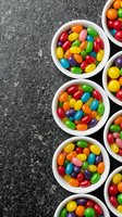 Colorful jelly beans candy in white bowls on dark stone surface for party treats and sweet confectionery displays.