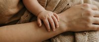 Tender moment of parent and child hands touching, showing love, care and family connection on cozy knitted sweater background.