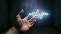 Hand holding a glowing sound wave with colorful light energy above the palm on a dark background, symbolizing technology and innovation.