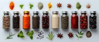 Colorful spices and seasonings in glass jars arranged in row with fresh herbs and whole ingredients on light background, culinary flat lay composition.