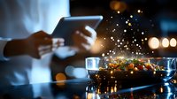 Hands holding digital tablet near steaming pan with fresh stir fry dish in dark kitchen interior with bokeh lights and steam creating atmospheric mood.