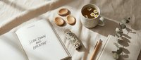 Cozy morning flat lay with open journal, herbal tea cup, wooden bowls and eucalyptus branch on neutral linen creating peaceful workspace atmosphere.