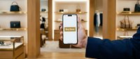 Hand holding smartphone with Buy Now button in luxury fashion boutique, showcasing mobile shopping and e-commerce retail experience.