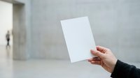 Young adult with medium skin tone holding blank white card or paper in modern minimalist interior space, suitable for business messaging, marketing campaigns, and corporate communications.