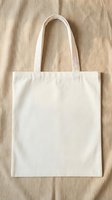 Blank white cotton tote bag on natural linen fabric background, eco-friendly reusable shopping bag mockup for custom design and branding projects.