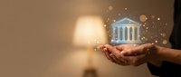 Businessman holding glowing bank building hologram with golden particles representing digital banking, financial services and modern investment solutions.