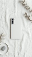 White smartphone with protective case on marble surface surrounded by eucalyptus leaves and coffee cup in minimalist flat lay composition for lifestyle branding.