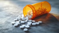 Prescription medication pills spilling from orange pharmacy bottle on textured concrete surface in dramatic lighting, medical and healthcare concept.