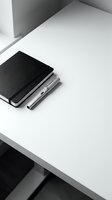 Minimalist black notebook and silver pen on clean white desk surface in modern office workspace for business planning and professional writing.