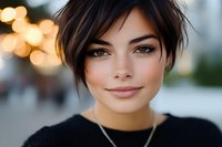 Young woman with short dark hair and fair complexion wearing black sweater, golden hour bokeh background, portrait for lifestyle and beauty content.