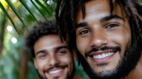 Young African American men with dreadlocks and natural hairstyles smiling genuinely at camera, showing joy and friendship against tropical foliage background.