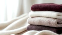 Stack of folded cozy knitted sweaters in neutral beige, white and burgundy colors on light background, soft focus. Warm autumn winter clothing concept.