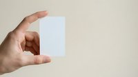 Male hand holding blank white card or paper against neutral beige background, suitable for business branding, mockup, and marketing materials.
