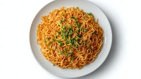 Asian style stir fried noodles garnished with fresh chopped green onions served on round white ceramic plate, top view on white background.