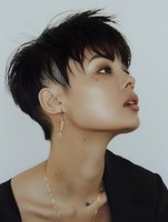 Young Asian woman with short pixie haircut and silver jewelry looking up against light background, profile view showing defined features and natural makeup.