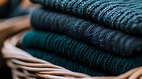 Neatly folded warm knitted sweaters in dark green and charcoal gray colors stacked in wooden drawer, cozy winter wardrobe essentials for cold weather season.