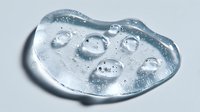 Transparent gel substance with water droplets on irregular shaped surface, isolated on white background for cosmetic product advertising.