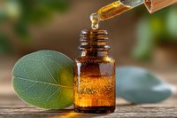 Essential oil dropping from glass pipette into amber bottle with fresh green leaf on wooden surface against blurred natural background. Aromatherapy concept.