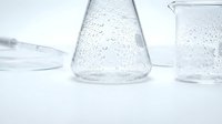 Clear glass laboratory beakers with water droplets on white background for scientific research and chemistry education experiments.