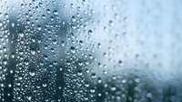 Water droplets on glass surface creating abstract pattern with blurred background for weather and nature concepts.