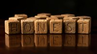 Wooden letter blocks spelling HONEST on reflective surface with warm lighting. Business ethics, integrity, trust concept for corporate presentations.