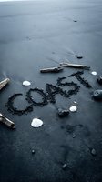 Word COAST written in dark volcanic sand surrounded by driftwood, white shells, and pebbles on a moody black beach shore.