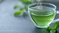 Steaming green tea in transparent glass cup with fresh mint leaves on gray background, aromatic hot beverage with rising vapor creates calming atmosphere.