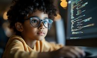 Young African American child with glasses and curly hair focused on computer screen displaying programming code in dark room.