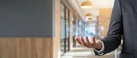 Businessman in dark suit holding glowing digital network icons in modern office corridor with warm lighting, representing connectivity and technology solutions.