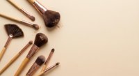 Professional makeup brushes with wooden handles arranged on neutral beige background for beauty and cosmetics applications.