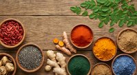 Colorful spices and superfoods in wooden bowls on rustic table with fresh herbs, ginger and turmeric root for healthy cooking and natural medicine.