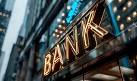 Glowing neon bank sign illuminated at dusk against urban building facade with bokeh lights creating modern financial district atmosphere.