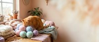 Orange tabby cat sitting among colorful yarn balls on cozy windowsill with knitting supplies and houseplants in warm sunlit room for crafting projects.