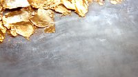 Luxurious gold leaf flakes scattered on textured gray concrete surface, creating elegant contrast between metallic and industrial elements. Copy space below.