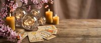Mystical fortune telling setup with tarot cards, crystal balls, burning candles and cherry blossoms on rustic wooden table for spiritual guidance sessions.