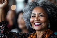 Mature African American woman with natural gray curly hair smiling confidently, wearing orange patterned clothing and burgundy lipstick against blurred background.