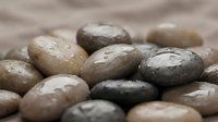 Smooth polished river stones in natural earth tones with water droplets creating zen spa atmosphere for meditation and wellness concepts.
