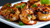 Grilled jumbo shrimp with caramelized glaze and fresh herbs served on white plate, close up view showing juicy texture and char marks from cooking.