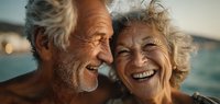 Happy senior couple laughing together at sunset by the sea, enjoying retirement and romantic moment with natural light and ocean backdrop.