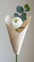 Single white ranunculus flower wrapped in minimal cream paper cone with eucalyptus leaves against neutral background, elegant floral composition for wedding and gift design.