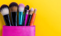 Colorful makeup brushes in bright pink holder against vibrant yellow background. Professional beauty tools for cosmetic application and face contouring. Minimal style composition.