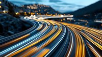 Long exposure of curved highway at dusk showing light trails from vehicles against mountain landscape with city lights in background, moody evening atmosphere.