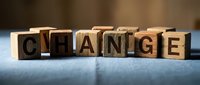 Wooden letter blocks spelling CHANGE on blue surface with warm lighting. Business transformation and personal development concept for motivational content.